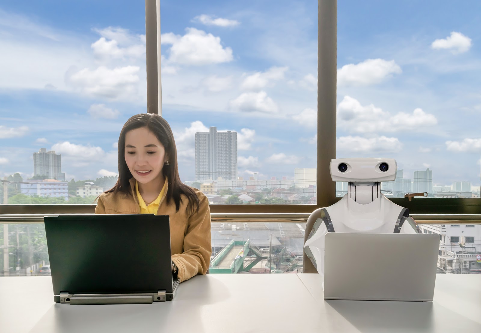 Woman and robot typing on laptops